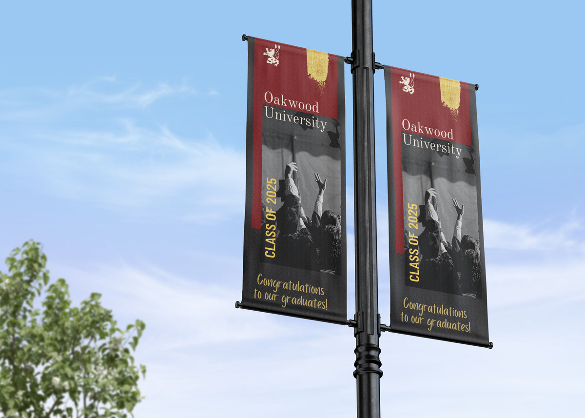 Two Oakwood University graduation banners on a pole against a blue sky.