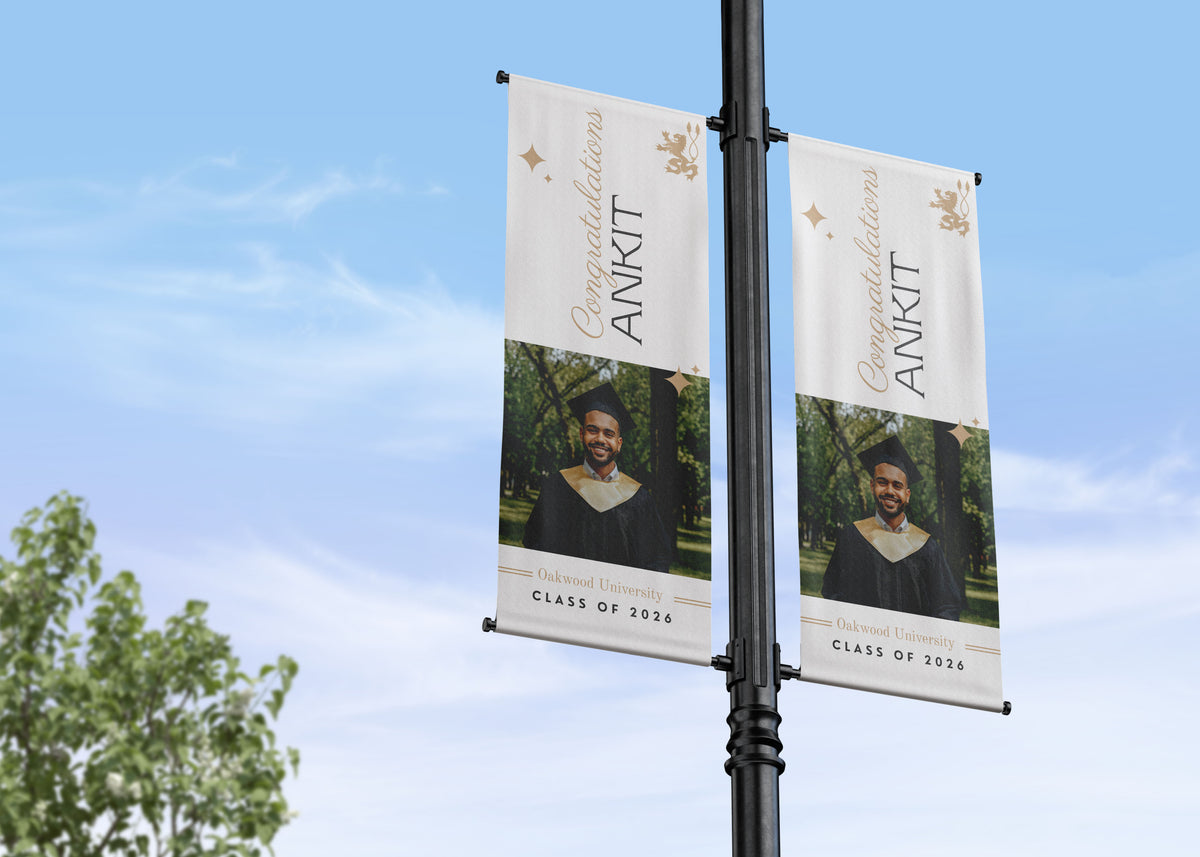 Two graduation-themed banners on a pole against a blue sky with trees.