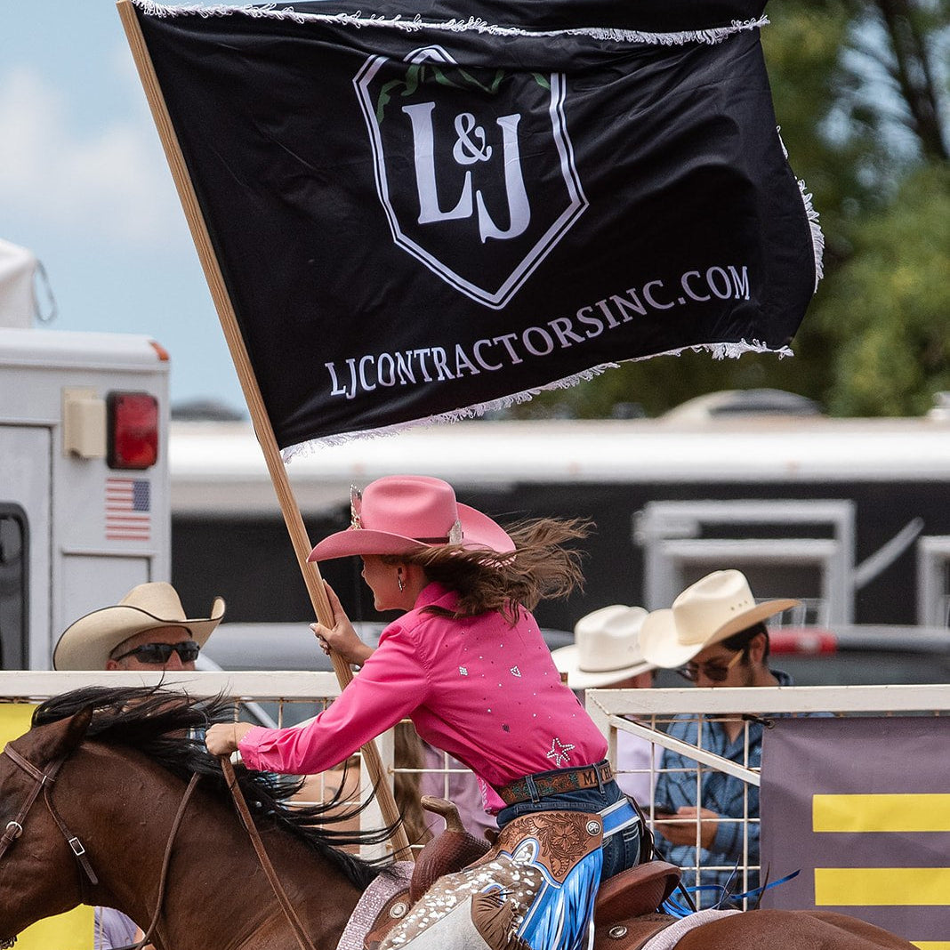 Cowgirl riding a bucking horse with L&J Contractors Inc. flag in the background