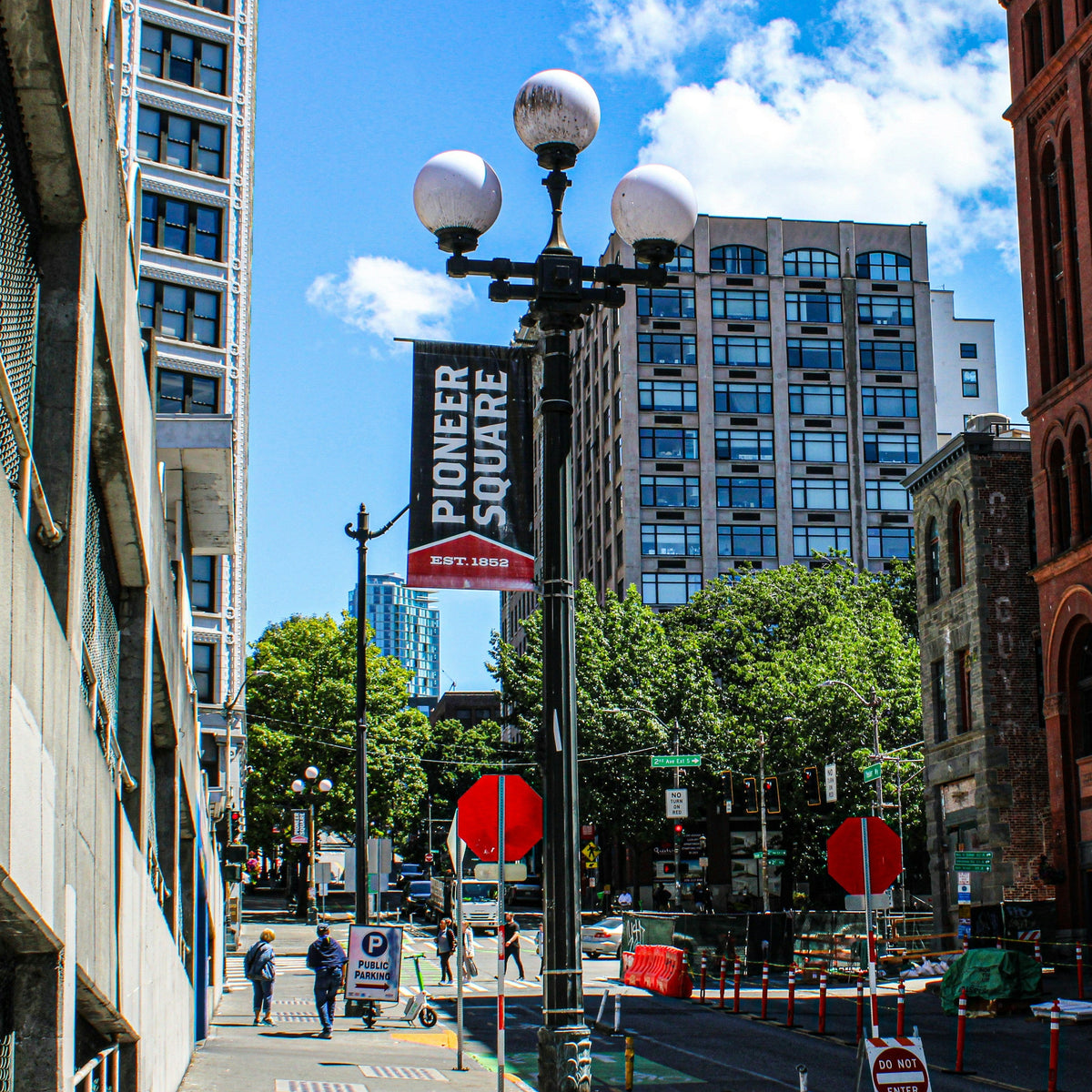 City street scene with buildings, street signs, and pedestrians under a blue sky.